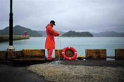 7月6日，韓國(guó)珍島，一名海岸警察在港口系救生圈。4月，客輪在珍島近海發(fā)生沉船事故后，仍有11人下落不明。