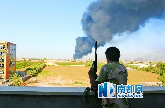 2日，利比亞首都的黎波里，一民兵武裝成員眺望被火箭彈擊中的儲油罐冒出濃煙。