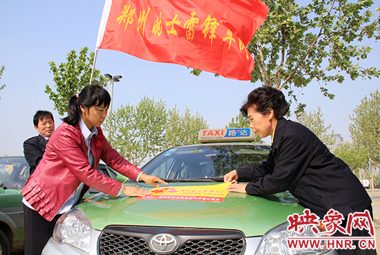 　　授旗結(jié)束后，首都的士雷鋒車隊(duì)王鳳進(jìn)隊(duì)長（右）與鄭州的的哥的姐在車身上貼上標(biāo)識(shí)。