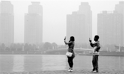 29日中午，鄭東新區(qū)如意湖畔，兩個(gè)年輕人拍攝霧霾中的景色。 鄭州晚報(bào)記者 馬健 圖