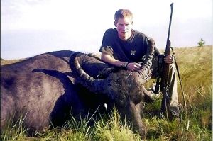 哈里王子手持獵槍，蹲在一頭遭到獵殺的水牛旁邊
