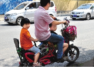 周先生騎著一輛低矮的電動車帶著一對兒女，很不安全。