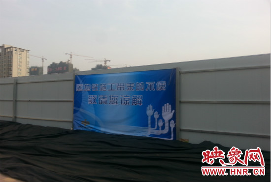 道路南側(cè)圍起了白色的圍擋，墻上標(biāo)示著“因地鐵施工帶來的不便敬請您諒解”的提示牌。