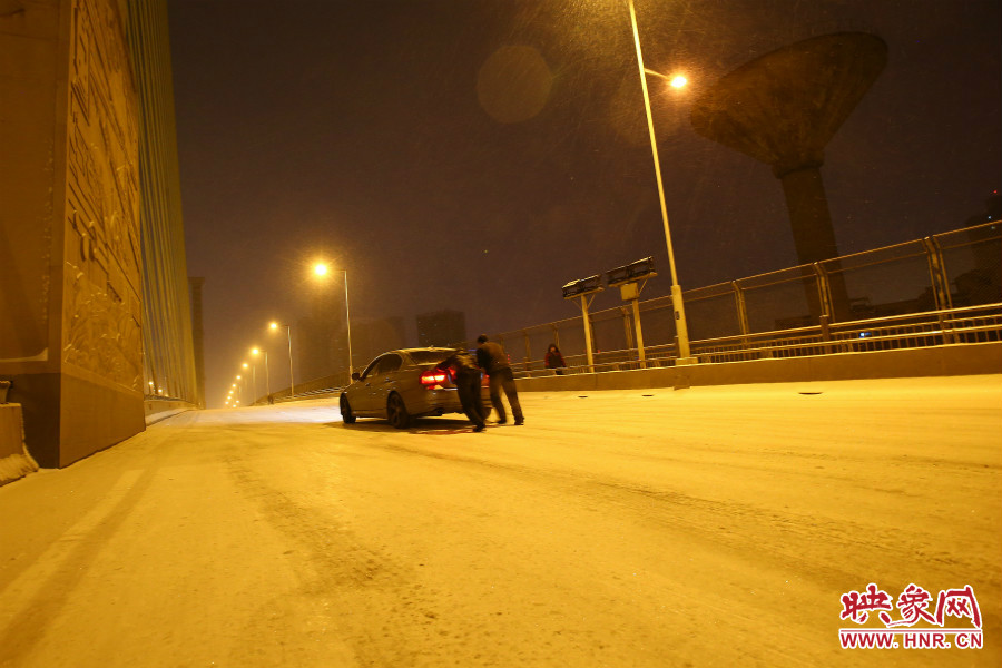 雪天路滑，汽車(chē)上橋打滑，兩名“推車(chē)人”幫助一輛私家車(chē)上坡。