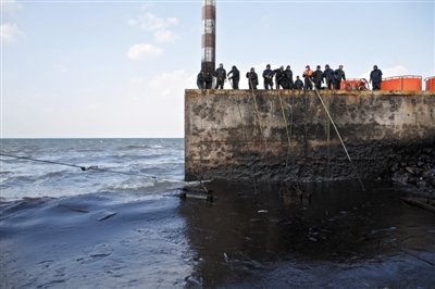 昨日，山東青島，清污人員正在海邊清理油污。