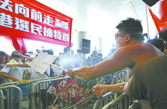 17日，在香港立法會(huì)外，一名反對(duì)政改的男子向支持派人群投擲標(biāo)牌。