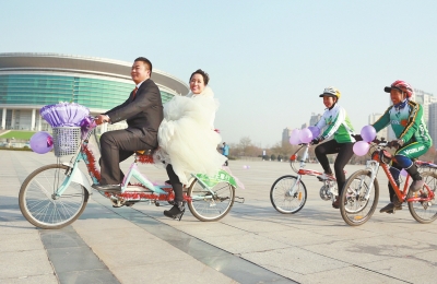 氣球和鮮花裝點(diǎn)的雙人自行車，新郎郝幸福載著美麗新娘回家。